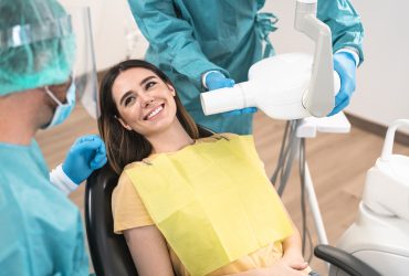 Man dentist operating young smiling woman in dental clinic - Oral heathcare assistance concept